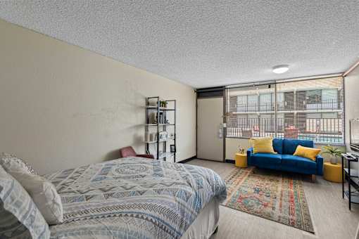 A bedroom with a bed, a blue couch, and a window with a view of a balcony.