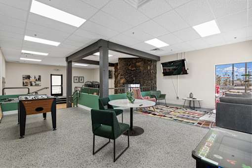 A room with a foosball table, chairs, and a television.