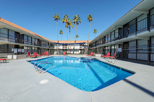 A swimming pool surrounded by red chairs and palm trees.