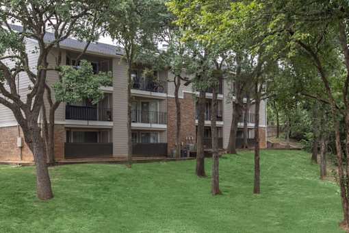 Apartment complex with green grass and trees in front.