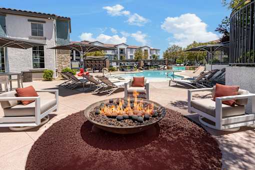 A patio with a fire pit and chairs.