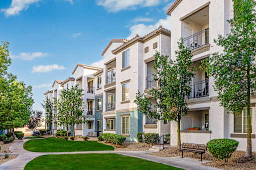 A row of apartment buildings with balconies and trees in front.