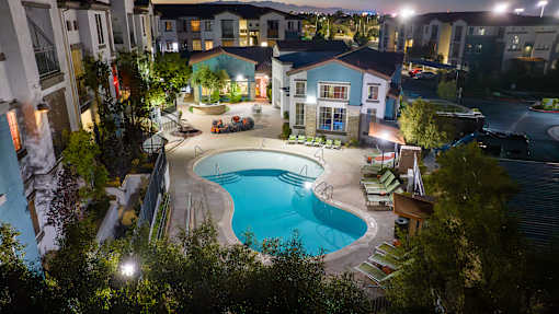 A swimming pool surrounded by a patio area and trees at night.