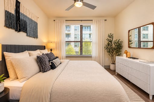 A bedroom with a large bed, a ceiling fan, and a window with blinds.