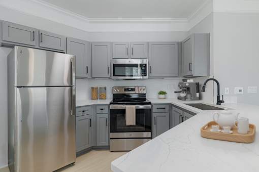 A modern kitchen with a stainless steel refrigerator and a wooden tray with tea cups on the counter.