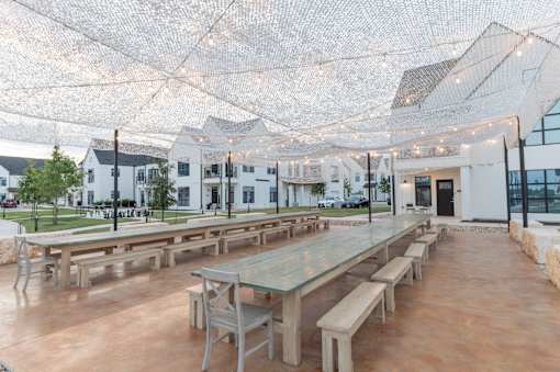 A large outdoor dining area with tables and benches under a net of lights.