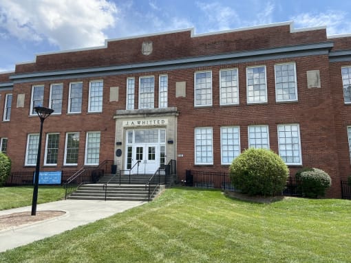 the front of a brick building with a lawn and steps