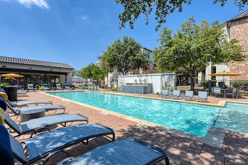 A pool surrounded by lounge chairs and trees.