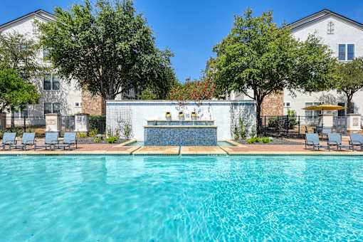 A swimming pool surrounded by trees and chairs.