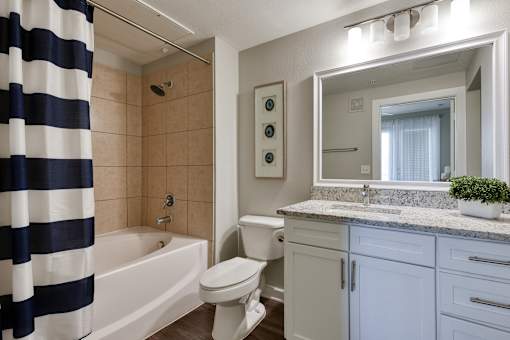 A bathroom with a white toilet, a white sink, and a white bathtub with a blue and white striped shower curtain.