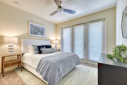 A bedroom with a bed, a ceiling fan, and a painting on the wall.