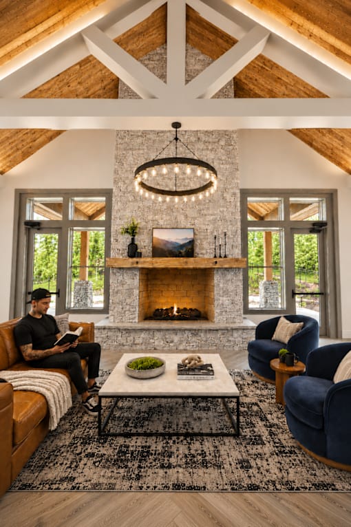 A man is sitting on a brown couch in a room with a stone fireplace and a chandelier.