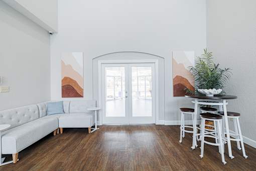 A white couch with a blue pillow is in front of a painting in a room with a wooden floor.