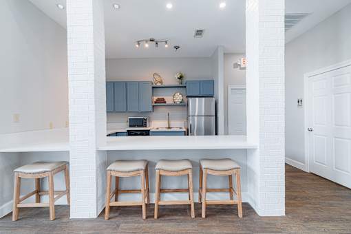 A kitchen with white walls and a white counter top with three stools.