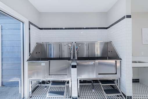 A clean, empty commercial kitchen with stainless steel appliances and white tiled walls.