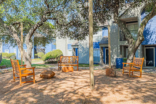 A sunny day at a park with wooden chairs and trees.