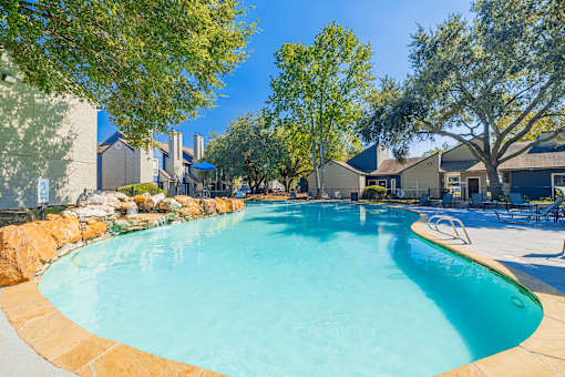 A large outdoor swimming pool surrounded by trees and a stone wall.