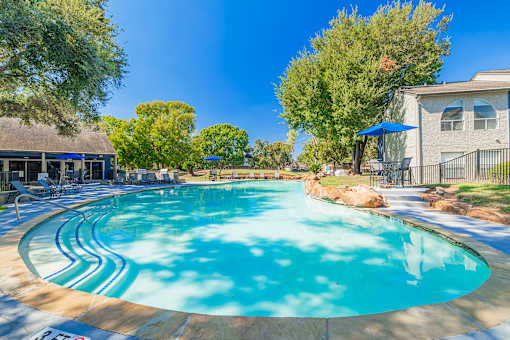 A large outdoor swimming pool surrounded by trees and a building.