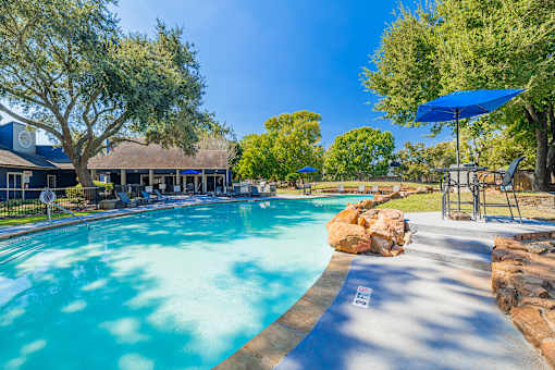 A swimming pool surrounded by trees and a blue umbrella.