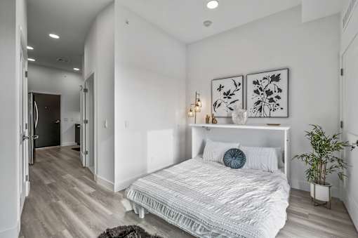 A bedroom with a bed, a plant, and two framed pictures on the wall.