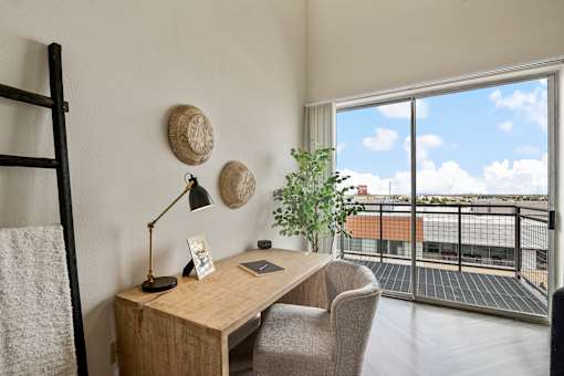 A room with a desk and chair with a window overlooking a balcony.