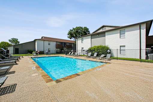A swimming pool surrounded by chairs and a fence in front of a building.