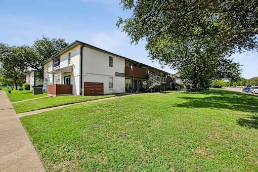 A white building with a brown roof is surrounded by a green lawn.