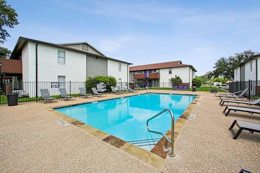 A swimming pool surrounded by lounge chairs and apartment buildings.