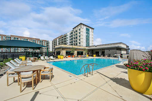 A pool area with a table and chairs and a building in the background.