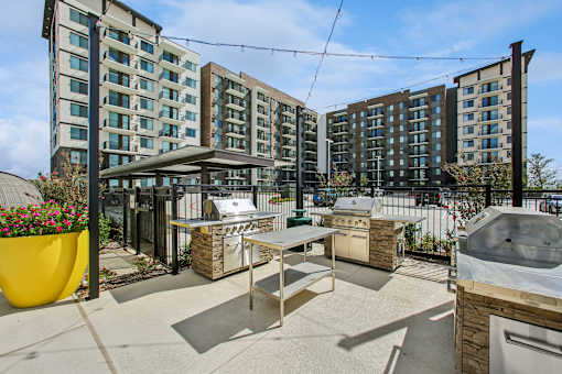 A patio area with a hot tub, barbecue grill, and seating area in front of apartment buildings.