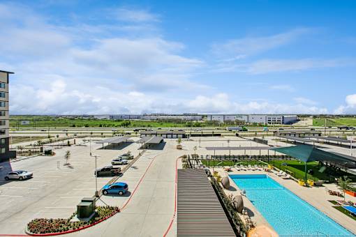 A large outdoor swimming pool is surrounded by a parking lot and buildings.