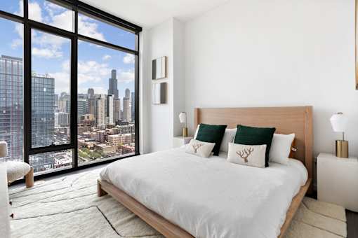 A bedroom with a large bed and a view of the city skyline.