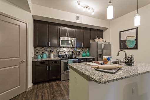 A kitchen with a granite countertop and dark brown cabinets.