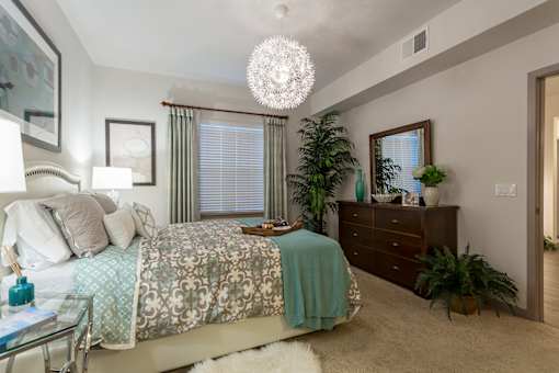 A bedroom with a bed, dresser, and plants.