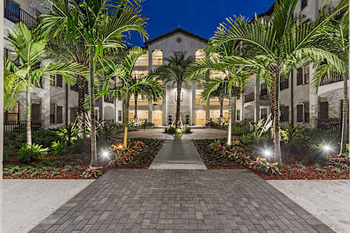 A building with a pathway and palm trees in front.