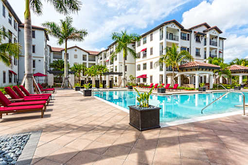 A pool surrounded by red chairs and palm trees.