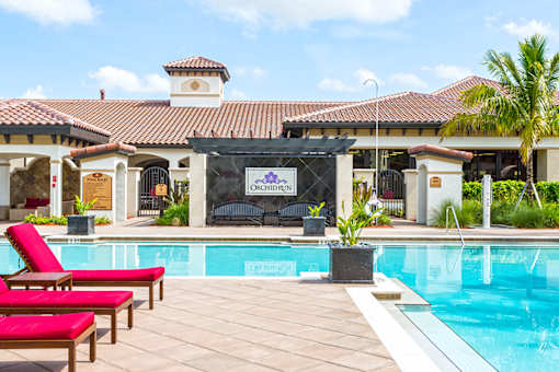 A poolside area with red lounge chairs and a building in the background.