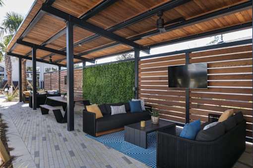 A patio with a black couch and a TV mounted on a wooden wall.