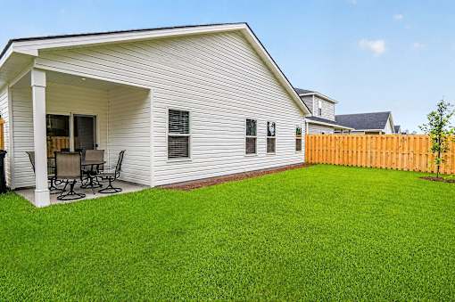 A white house with a covered patio and a green lawn.