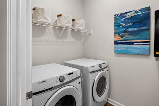 A white Samsung washing machine sits in a laundry room next to a dryer.