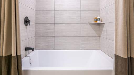 A white bathtub in a bathroom with beige tiles and a beige shower curtain.