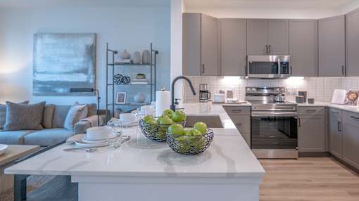 A modern kitchen with a white island and a bowl of green apples on it.