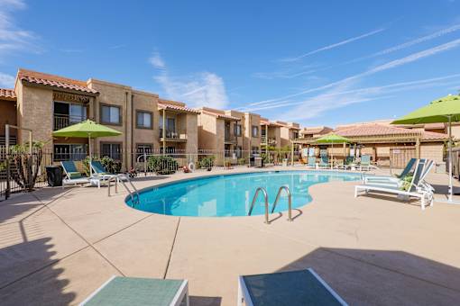 A swimming pool surrounded by lounge chairs and umbrellas in a sunny day.