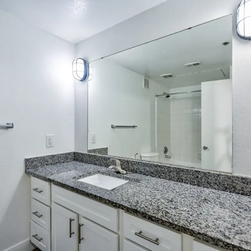A bathroom with a granite countertop and white cabinets.