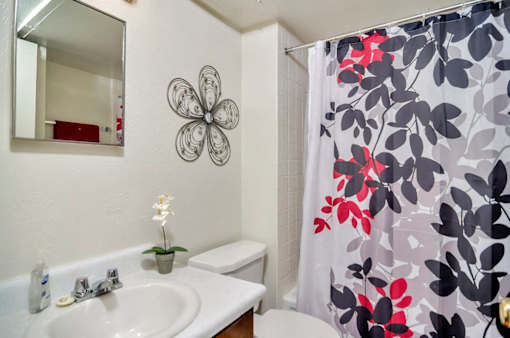 A white sink with a flower on the wall and a shower curtain with a flower design.
