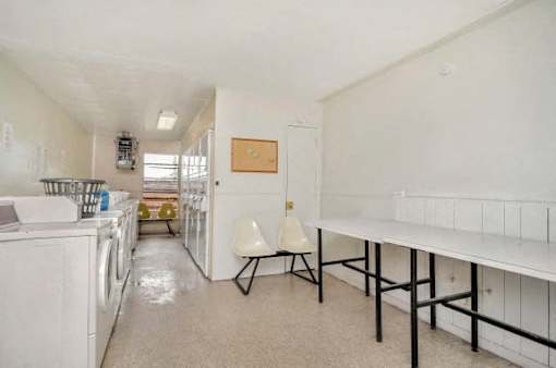 A laundry room with a white washer and dryer, a white chair, and a white table.