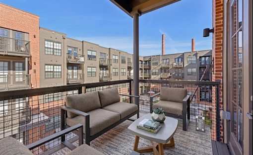 A balcony with a couch, chairs, and a table with a pineapple on it.