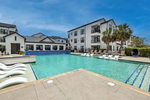 A large swimming pool with lounge chairs and a building in the background.