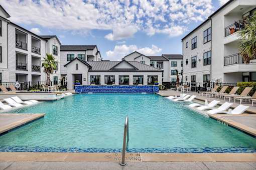 A pool surrounded by lounge chairs and buildings in the background.