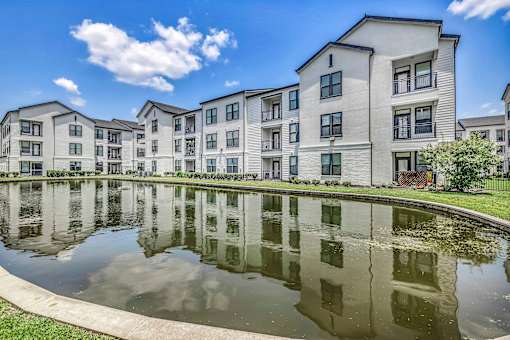 A row of modern apartment buildings is reflected in a pond.
